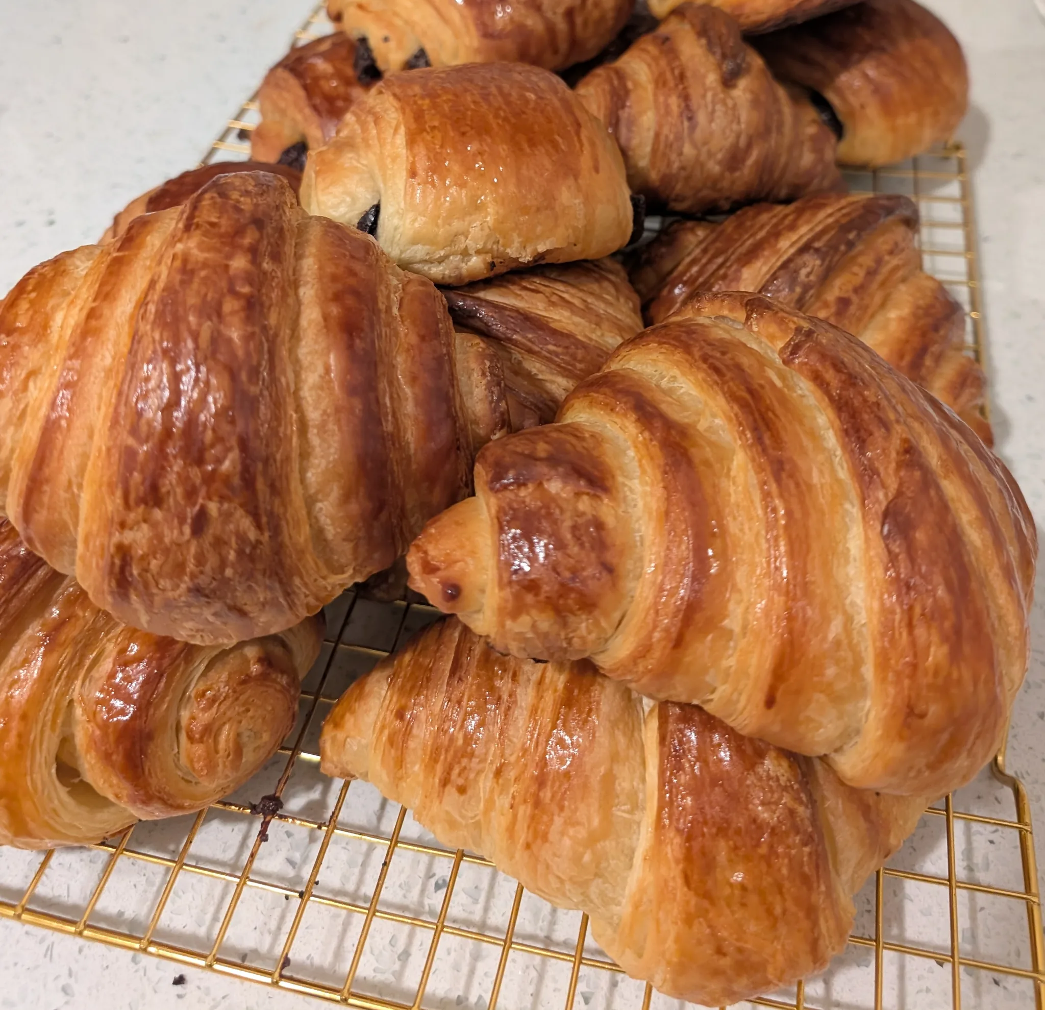 A golden cooling rack piled high with freshly baked croissants and pains au chocolat
